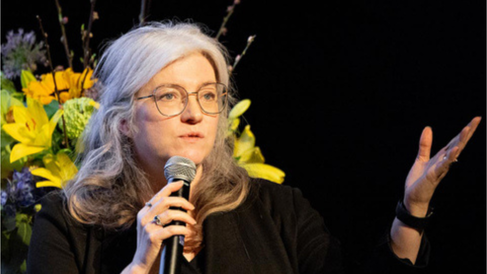 Photo of Thora Karadottir speaking onstage with a bouquet behind her