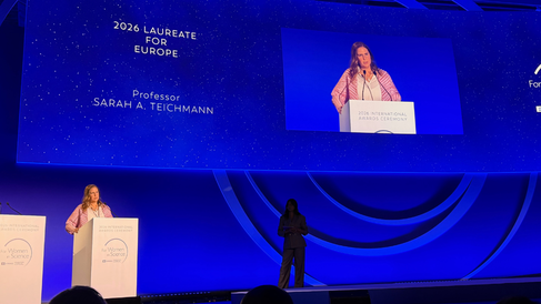 Blue-lit stage with Sarah Teichmann at lectern accepting an award. In the background, a zoomed-in image of Sarah and the the words 2026 'Laureate for Europe'