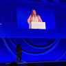 Blue-lit stage with Sarah Teichmann at lectern accepting an award. In the background, a zoomed-in image of Sarah and the the words 2026 'Laureate for Europe'