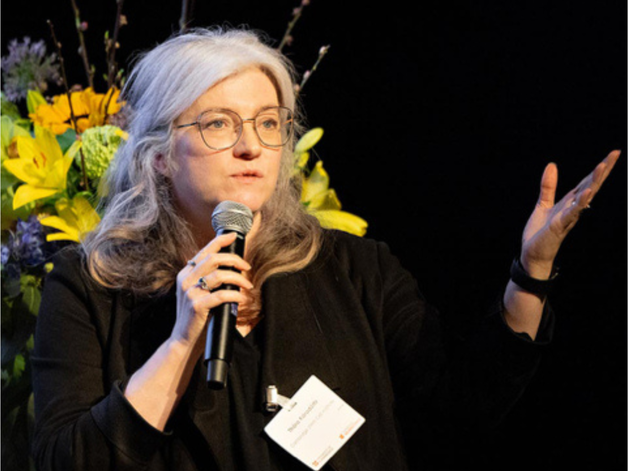 Photo of Thora Karadottir speaking onstage with a bouquet behind her