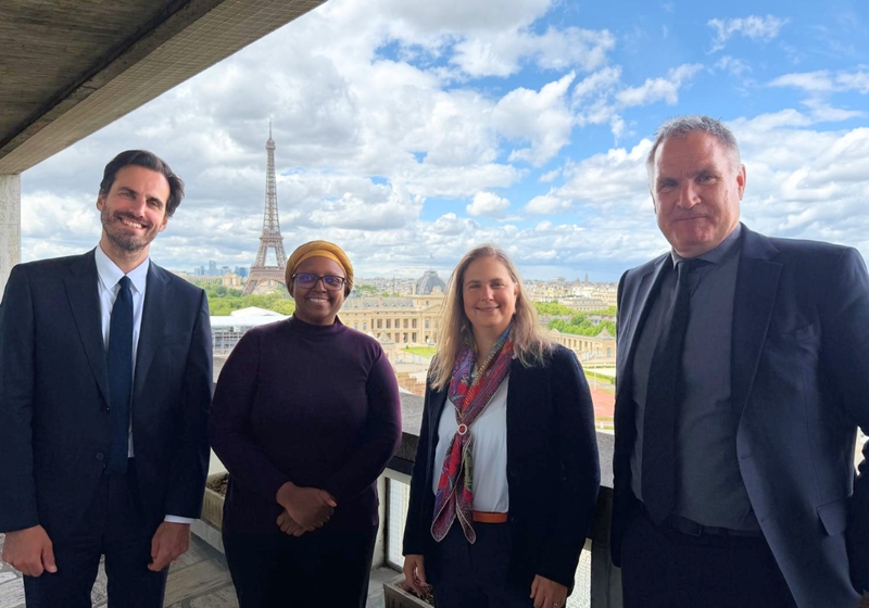 Sarah Teichmann pictured with ambassadors from UNESCO on a balcony, with a view of Paris and the Eiffel Tower behind them. 